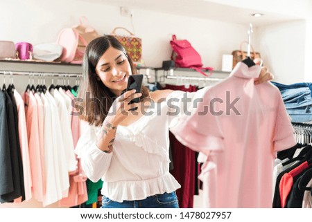 Trendy Hispanic woman photographing top at boutique in shopping mall