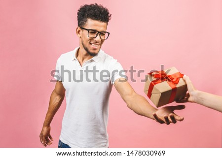 Cheerful smiling african american millennial guy in eyewear holding wrapped present box. Happy black young man congratulating, giving birthday gift, isolated on pink background.