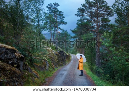 portrait of young traveler hold umbrella stay on road on of spellbinding landscape of Norwegian nature with high charming mountains and hills in which it is impossible not to fall in love