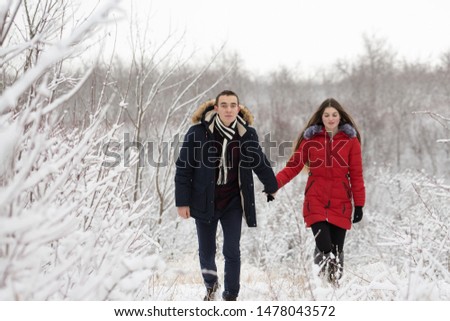 The guy and the girl have a rest in the winter woods. Husband and wife in the snow. Young couple walking in winter park