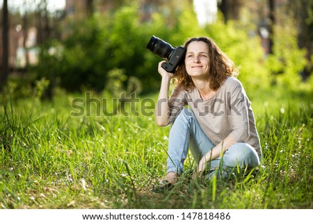 A woman with a camera sitting on the grass in the park.