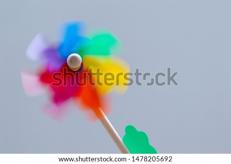 colorful plastic windmill rotate motion blur stick on light wooden against grey background 
