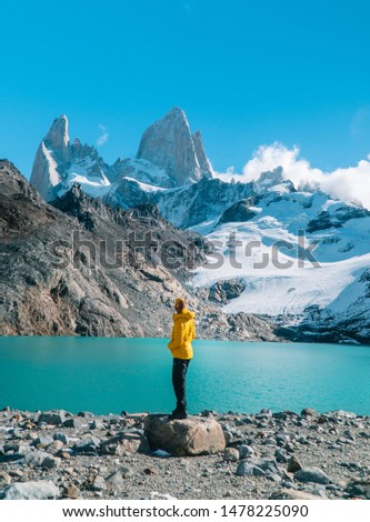 Tourist man & scenic view of snowcapped mountain tops of Mount Fitzroy, Patagonia trek. Blue sky, turquoise blue lake and scenic rock landscape. Shot in Argentina. Nature, travel, adventure, hiking.