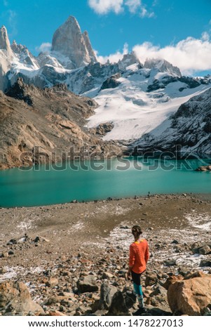 Tourist woman & scenic view of snowcapped mountain tops of Mount Fitzroy, Patagonia trek. Blue sky, turquoise blue lake and scenic rock landscape. Shot in Argentina. Nature, travel, adventure, hiking.