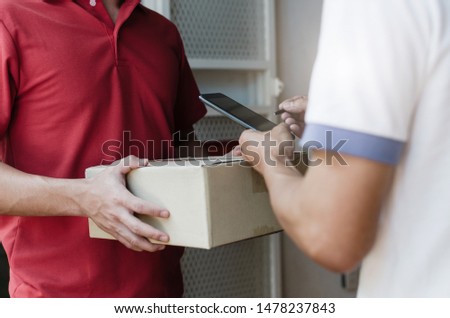 young man customer appending digital signature in mobile phone receiving parcel post box from courier with home delivery service man smiling face in red uniform at home, express delivery concept