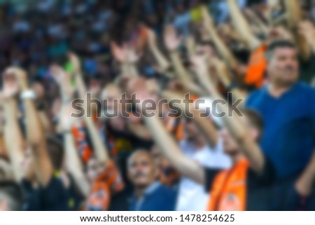 Out of focus, not sharp sport background - spectators at stadium. Crowds of fans in stands of football stadium during match Tribune with fans. Stands with football fans