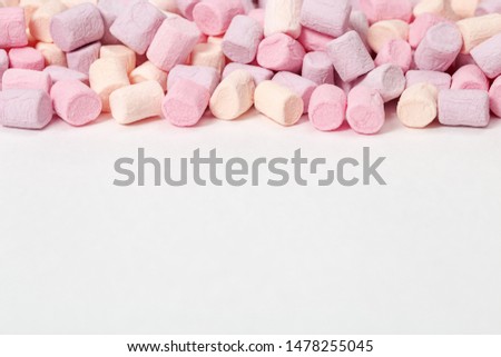 Gentle pink and yellow marshmallows on white paper background with copy space. Sweet food. Selective focus. Pastel color. 