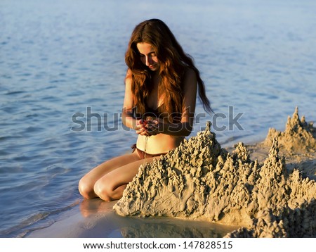 beautiful young girl builds a sand castle on the beach at sunset