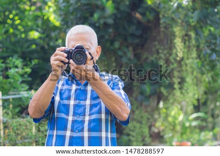 Senior man taking photo by digital camera in the garden. Elderly man wears a blue shirt, happy when using a camera. Photography concept. Space for text