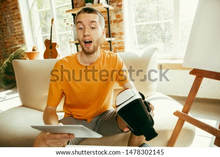 Young caucasian male blogger with professional equipment recording video review of VR glasses at home. Blogging, videoblog, vlogging. Man making vlog or live stream about photo or technical novelty.
