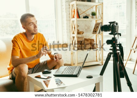 Young caucasian male blogger with professional camera recording video review of gadgets at home. Blogging, videoblog, vlogging. Man making vlog or live stream about photo or technical novelty.