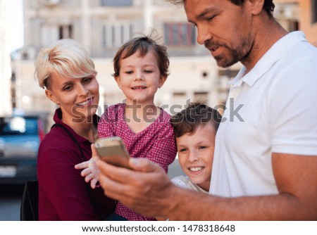 Young family with two small children standing outdoors in town, using smartphone.
