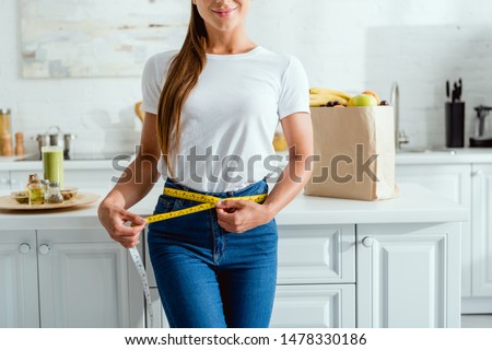 cropped view of happy young woman measuring waist near groceries  Royalty-Free Stock Photo #1478330186