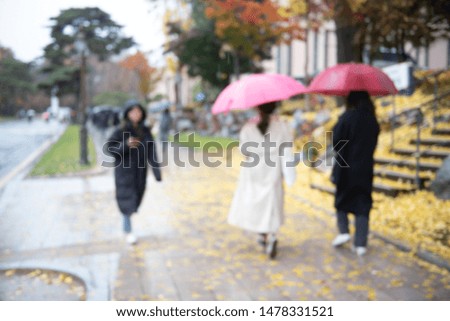Blurred of anonymous asian women with umbrella walking on sidewalk in autumn rainy day with colorful autumn leaves as background