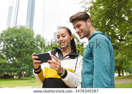 Photo of athletic smiling man and woman wearing sportswear using cellphone while working out in city park