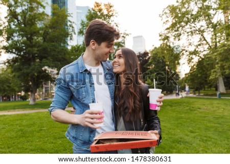 Picture of smiling young friends loving couple in nature green park outdoors eat pizza.