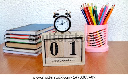 intermittent wooden calendar with the date of the first of September and an alarm clock, colored pencils on the table, a reminder of the school, close-up