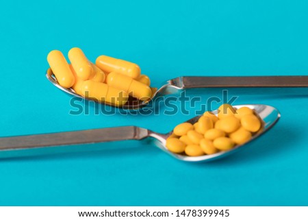 Table spoons filled with assortment of yellow pills isolated on blue  coloured background. Medication and prescription pills flat lay background. Antiobesity medication and dieting.
