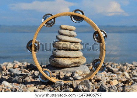 Musical instrument a tambourine and a pyramid of stones on the bank of the lake. Interesting picturesque background for a desktop.