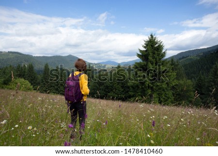tourist girl with a backpack and camera standing in the meadow at the mountains. 
