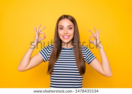 Portrait of cute pretty millennial in striped t-shirt showing ok sign advertising isolated over yellow background
