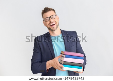 Handsome male teacher with books on light background