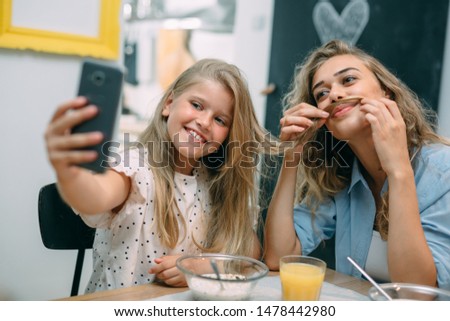 young girl taking picture while having breakfast with her mother at home