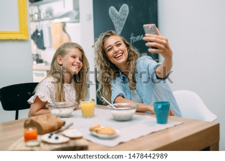 mother taking picture while having breakfast with her daughter at home