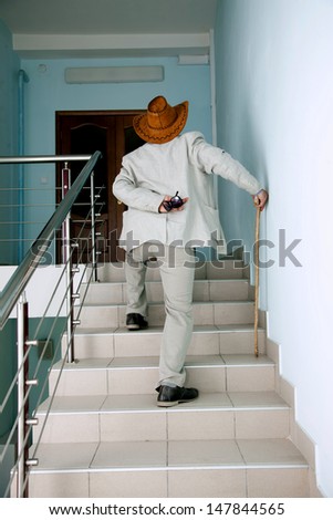 Old man climbs the stairs with the pain in his back and with stick