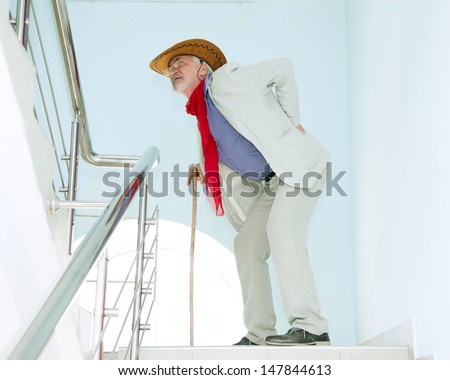 Old man climbs the stairs with the pain in his back and with stick
