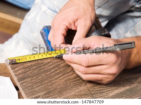 Man measuring a tile piece with a marker.The photo shows a detail of a construction job.