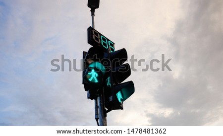 a green walking sign light/ pedestrian sign of traffic lights, shot in lower view with mixed blue-grey sky and clouds background