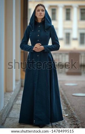 Poetic brown hair brunette sister beautiful woman girl vintage classic coat blue dress look camera green eyes hands together street old town outdoor blue sky river vaults building scenic windows view Royalty-Free Stock Photo #1478499515