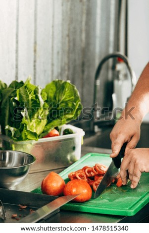 cropped view of cook cutting tomatoes on chopping board