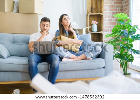 Young beautiful couple relaxing sitting on the sofa of new house using computer laptop serious face thinking about question, very confused idea