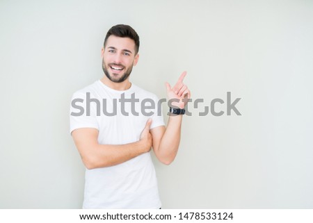 Young handsome man wearing casual white t-shirt over isolated background with a big smile on face, pointing with hand and finger to the side looking at the camera.