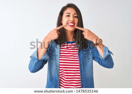 Young chinese woman wearing striped t-shirt and denim shirt over isolated white background smiling cheerful showing and pointing with fingers teeth and mouth. Dental health concept.