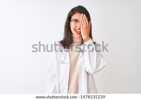 Chinese doctor woman wearing coat and pink stethoscope over isolated white background covering one eye with hand, confident smile on face and surprise emotion.