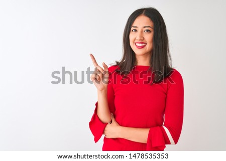Young beautiful chinese woman wearing red dress standing over isolated white background with a big smile on face, pointing with hand and finger to the side looking at the camera.
