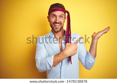 Hangover business man drunk and crazy for hangover wearing tie on head amazed and smiling to the camera while presenting with hand and pointing with finger.