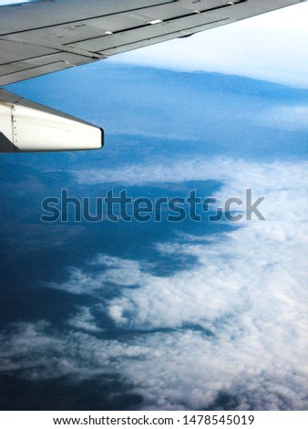 View from the airplane porthole on white clouds. The frame also shows the wing of the aircraft. Travel Photo.