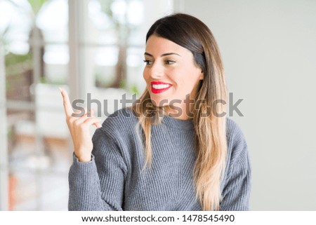 Young beautiful woman wearing winter sweater at home with a big smile on face, pointing with hand and finger to the side looking at the camera.