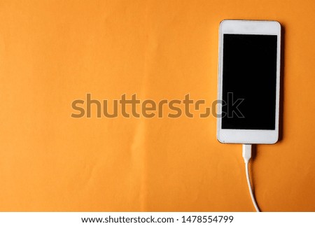 close up white Smartphone Plug In with Charger Adapter on orange Background