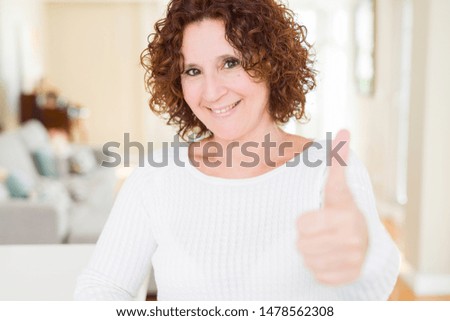Beautiful senior woman wearing white sweater doing happy thumbs up gesture with hand. Approving expression looking at the camera showing success.