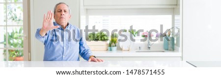 Wide angle perspective of handsome senior man at home doing stop sing with palm of the hand. Warning expression with negative and serious gesture on the face.