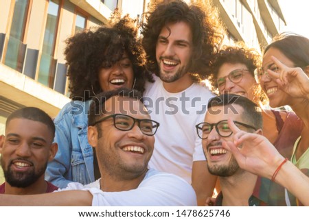 Joyful happy friends taking group selfie at sunset. Mix raced team of men and women posing, making peace gesture and smiling at phone camera. Selfie concept