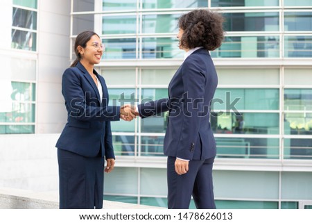 Two young women shaking hands near modern building. Closeup shot of two employees shaking hands and laughing. Business handshake concept