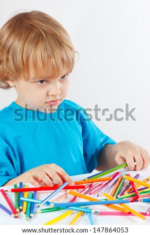Young blond boy at the table with color pencils on a white background