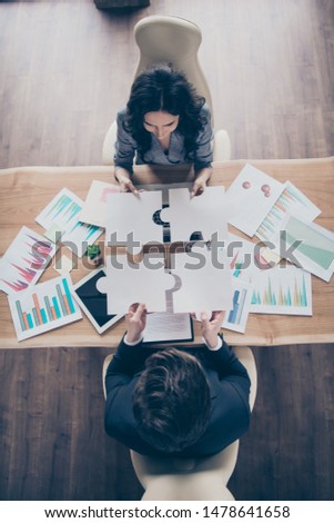 High angle view vertical photo of two partners putting difficult puzzle pieces together above workshop table