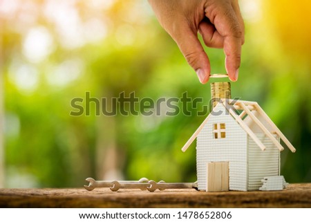 Man hand holding gold coin saving to build house and construction tools with repairing on sunlight in the public park, Loan for renovation to real estate and home decorating concept.